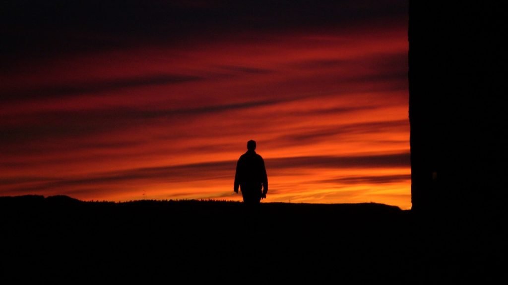 silhouette of man walking with orange sunset behind