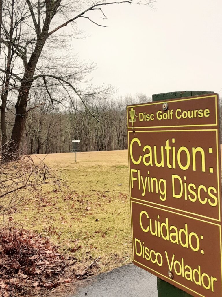 sign at FDR state park disc golf course reads Caution: Flying Discs and Cuidado, Disco Volador
