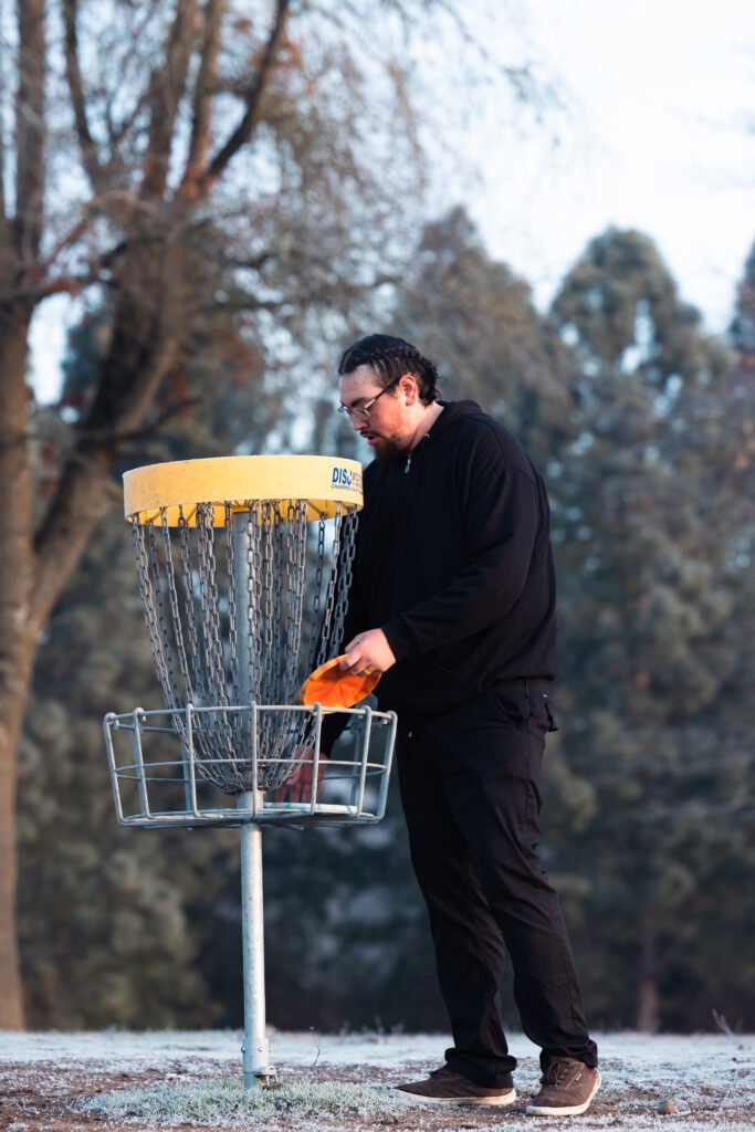 Tyee Rilatos collecting a disc from disc golf basket