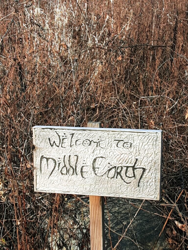 Sign saying Middle Earth in front of high grass