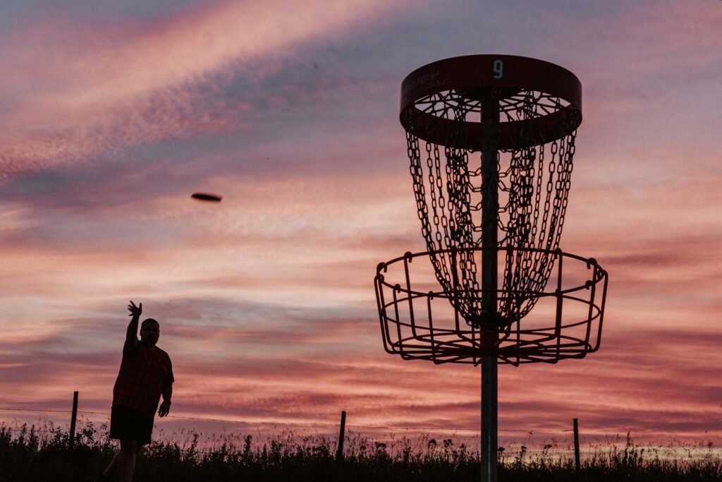 A silhouette of a man throwing a disc at a disc golf basket